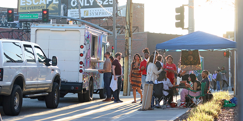 People walking down the street past food trucks at First Fridays